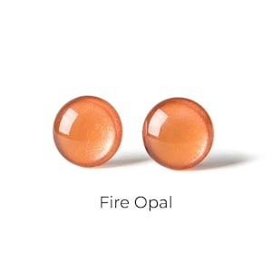May include: A pair of small, round, orange-colored earrings with a shimmery finish. The earrings are called "Fire Opal".