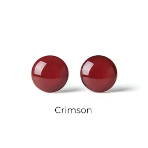 May include: Two crimson-colored, round stud earrings. The earrings are glossy and reflect light, set against a white background. The word "Crimson" is written in a simple font below the earrings.