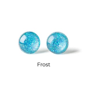Op de afbeelding: Twee ronde, helderblauwe oorstekers met glitter. De oorbellen zijn gemarkeerd met "Frost" in een zwarte lettertype. De oorbellen staan tegen een witte achtergrond.