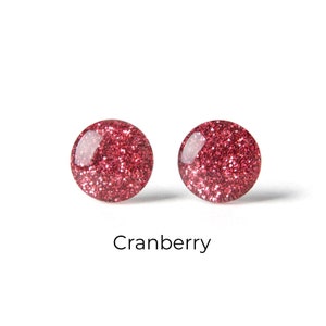 Könnte beinhalten: Ein Paar runde Ohrstecker mit einem Cranberry-roten Glitzerfinish.