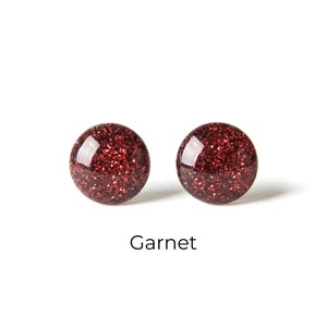 May include: A pair of red glitter stud earrings. The earrings are round and have a shiny finish.
