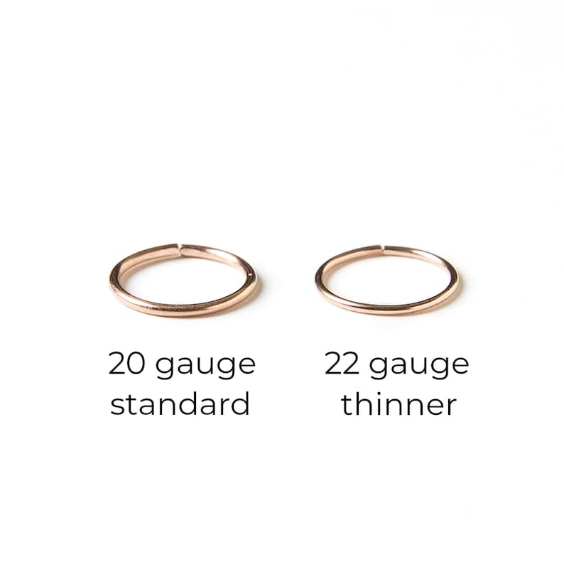 Puede incluir: Dos anillos de nariz, uno m&aacute;s grueso y otro m&aacute;s delgado, sobre un fondo blanco. El anillo m&aacute;s grueso est&aacute; etiquetado como "20 gauge standard" y el anillo m&aacute;s delgado est&aacute; etiquetado como "22 gauge thinner".