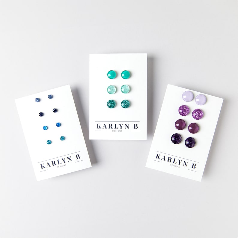 May include: Three sets of stud earrings on white cards. The first set is blue and teal, the second set is green and teal, and the third set is purple and lavender.