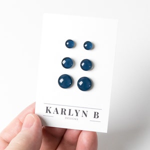 May include: Set of six blue glass stud earrings. The earrings are arranged in three rows of two on a white card with the text "KARLYN B DESIGNS".