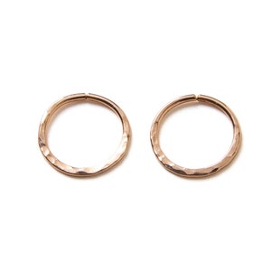 Puede incluir: Dos pendientes de aro de oro rosa martillados. Los aros son lisos y tienen una forma ligeramente irregular.