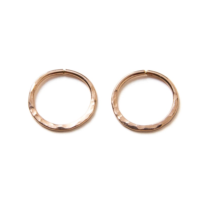 Puede incluir: Dos pendientes de aro de oro rosa martillados. Los aros son lisos y tienen una forma ligeramente irregular.