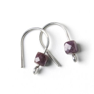 May include: A pair of silver hoop earrings with a dark purple gemstone on each earring.