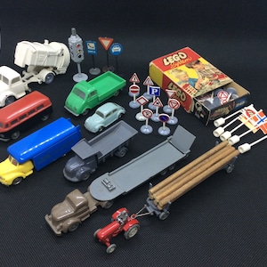 以下が含まれることがあります： 赤いバス、黄色のトラック、緑色のピックアップトラック、灰色のダンプトラック、灰色のフラットベッドトラック、赤いトラクター、白いゴミ収集車、白いバン、青い車、灰色の車など、ビンテージのおもちゃの車と交通標識のコレクション。このセットには、LEGO Systemの交通標識の箱も含まれています。