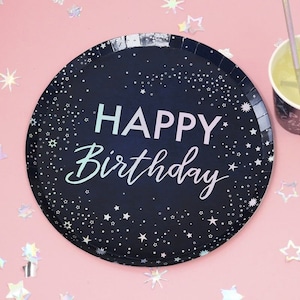Può includere: Un piatto di carta nero con un bordo argentato e un design a cielo stellato. Il piatto dice "Happy Birthday" in lettere rosa e bianche.