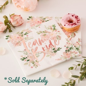 May include: A stack of white paper napkins with a floral design and the text "Team Bride" in rose gold foil.