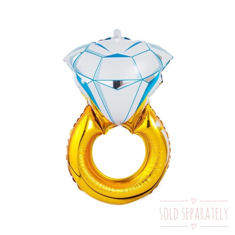 May include: A gold ring balloon with a large white diamond balloon on top. The balloons are shaped like a ring and diamond. The text "SOLD SEPARATELY" is printed below the balloons.