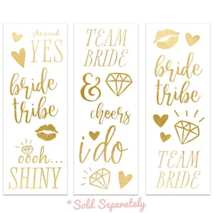 May include: Gold temporary tattoos with various phrases and designs, including "she said yes", "bride tribe", "team bride", "i do", "cheers", and "ooh shiny".