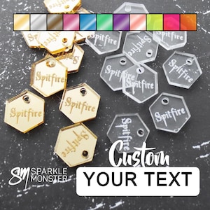 May include: Assortment of gold and clear acrylic hexagonal shaped tags with the word "Spitfire" engraved on each. The tags have a hole at the top for hanging. The text "Custom Your Text" is printed on a black background.