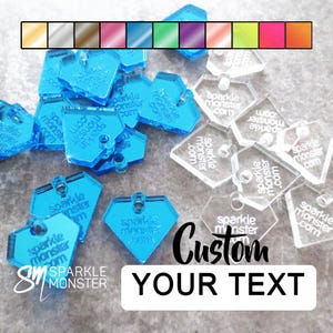 Könnte beinhalten: Eine Sammlung blauer und klarer Acryl-Anhänger in Diamant- und Sechseckformen. Jeder Anhänger hat ein kleines Loch zum Aufhängen und den Text "Sparkle Monster .com". Oben wird eine Farbpalette in verschiedenen Farbtönen angezeigt, unten steht "Custom Your Text".