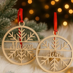May include: Two wooden Christmas ornaments with snowflake designs and red ribbon hangers. One ornament says "Mason" and the other says "Ava". The ornaments are circular and made of light-colored wood.