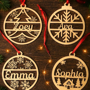 May include: Wooden Christmas ornaments with names Zoey, Ava, Emma, and Sophia. Each ornament is round with a decorative design and a red ribbon for hanging. The ornaments are on a dark wood surface with Christmas decorations.