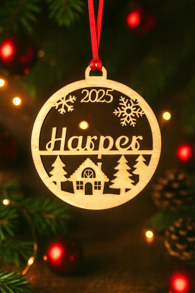 May include: A wooden Christmas ornament with a red ribbon. The ornament is circular with the name "Harper" and the year "2025" cut out. It features snowflake and tree designs, and a house silhouette.
