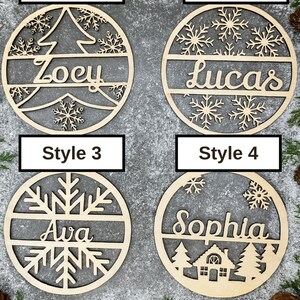 May include: Four wooden Christmas ornaments with personalized names. Style 1 features a tree design with the name "Zoey". Style 2 has snowflakes and the name "Lucas". Style 3 has a snowflake design with the name "Ava". Style 4 has a house design with the name "Sophia".