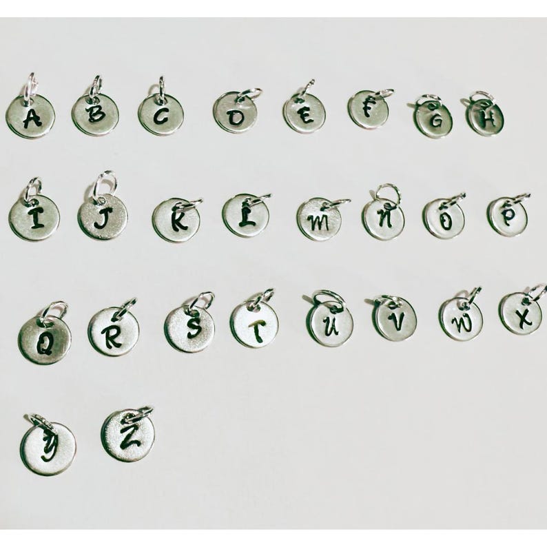 May include: A selection of small, silver-coloured alphabet charms, each with a loop for attaching to a necklace or bracelet. The letters A to Z are displayed in a clear, readable font. These charms are ideal for personalised jewellery.