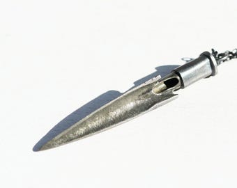May include: A silver-toned pendant necklace featuring a stylized arrowhead design. The pendant has a textured surface and a hollowed-out section. The necklace chain is a dark, linked style. The pendant is approximately 2 inches long.