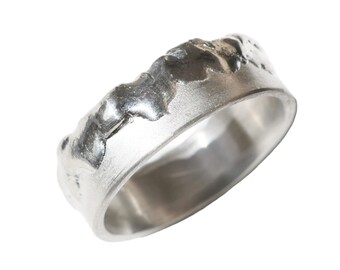 May include: A silver ring with a textured, organic design. The ring's surface has a rugged, uneven appearance, with a smooth interior band. The ring is likely made of sterling silver or a similar metal.