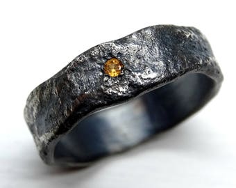 May include: A black metal ring with a textured finish and a small, yellow gemstone set in the center.