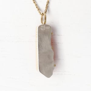 May include: A silver pendant necklace with a red and white agate stone. The pendant is attached to a gold chain. The back of the pendant is stamped with the text "HK 925".