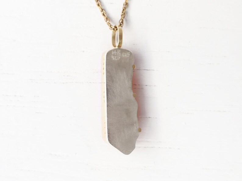 May include: A silver pendant necklace with a red and white agate stone. The pendant is attached to a gold chain. The back of the pendant is stamped with the text "HK 925".