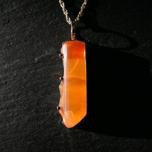 May include: A gold chain necklace with a pendant featuring a large, orange, translucent gemstone. The gemstone has a unique, swirling pattern.