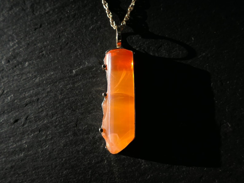 May include: A gold chain necklace with a pendant featuring a large, orange, translucent gemstone. The gemstone has a unique, swirling pattern.