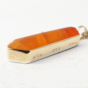 May include: A gold pendant necklace with an orange crystal shaped like a long, thin point. The pendant is set in a gold frame and has a detailed design.