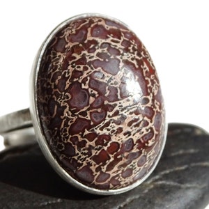 May include: A silver ring with a large oval-shaped red and white jasper stone set in a bezel setting.