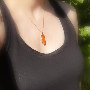 May include: A gold chain necklace with a long, rectangular orange pendant.