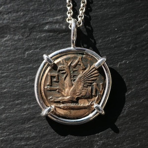 May include: Silver chain necklace with a pendant featuring a bronze coin depicting a winged creature with the Greek letters 'ΓΡ' and 'Ν' on either side.