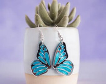 May include: A pair of silver butterfly earrings with turquoise blue enamel. The butterfly wings have a detailed design.