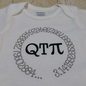 May include: White baby onesie with a black circle containing the text "QTTπ" and a gray circle around it with the digits of pi in gray.