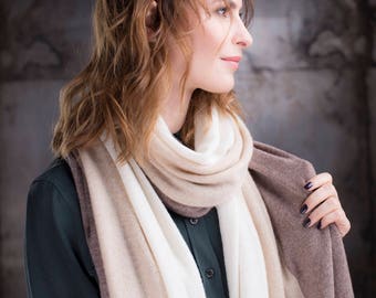 May include: A woman wearing a black shirt with a long, striped scarf in shades of beige and brown. The scarf is draped around her neck and shoulders.