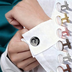 May include: A person wearing a white dress shirt with a cufflink featuring a black and white photo of a couple. Additional cufflinks in silver, gold, rose gold, brown, and silver are displayed.
