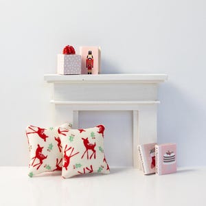 May include: Two red and white throw pillows with a reindeer and holly pattern, a white mantel with two wrapped gifts and a nutcracker figurine, and three miniature books with Christmas themes.