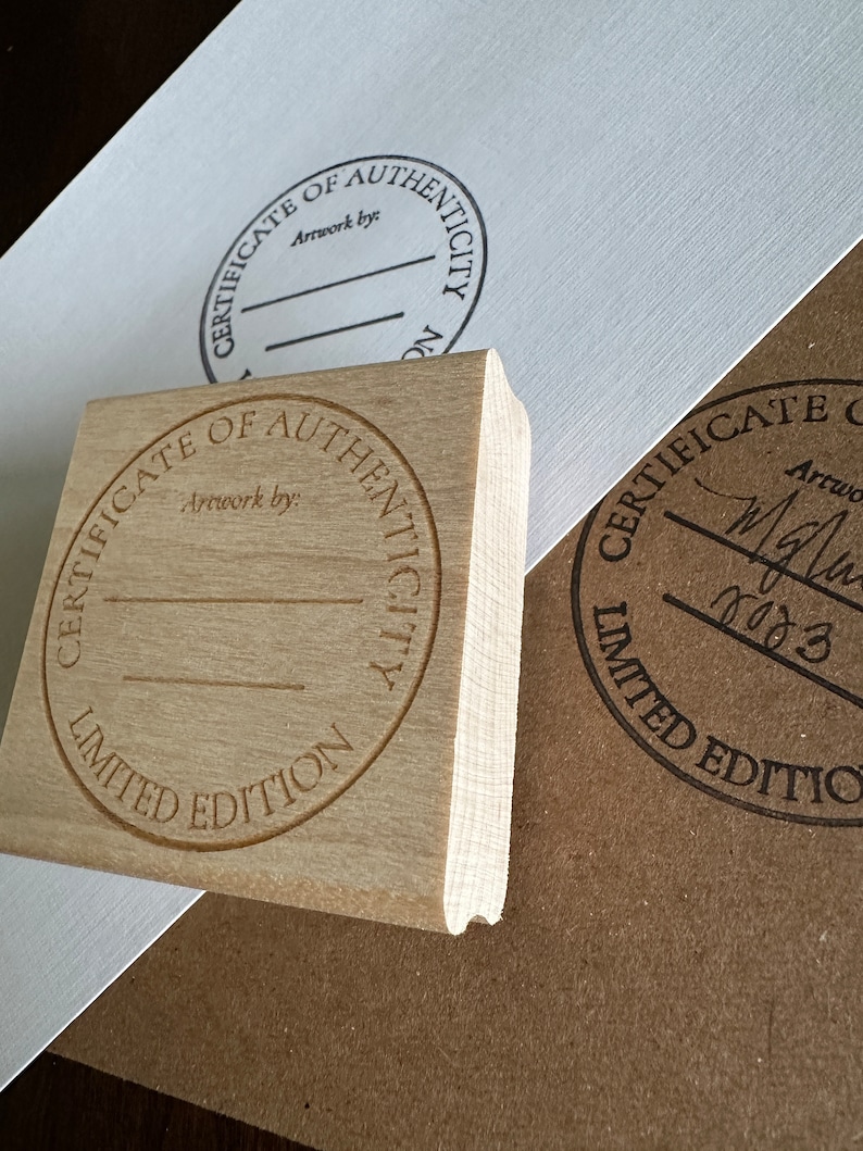 May include: Two wooden stamps with circular designs. The top stamp reads "Certificate of Authenticity Artwork by" and the bottom stamp reads "Certificate of Authenticity Limited Edition".