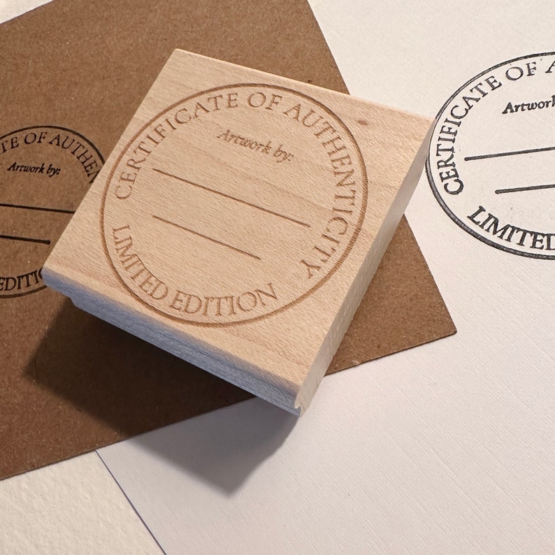 May include: A wooden stamp with a round design that says "Certificate of Authenticity Limited Edition". The stamp has two lines for writing in the center.