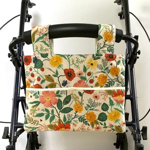 Puede incluir: Bolsa para andador con estampado floral con fondo crema, con amapolas rojas, margaritas amarillas y hojas verdes. La bolsa tiene dos bolsillos delanteros y correas para sujetar a un andador. La tela tiene un dise&ntilde;o bot&aacute;nico.