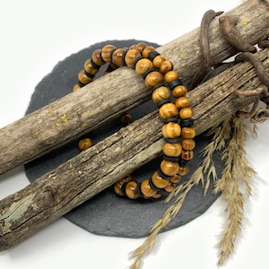 Könnte beinhalten: Ein Holz-Armband mit braunen und schwarzen Perlen. Das Armband wird auf einem Stück Treibholz und einer Schieferplatte präsentiert.