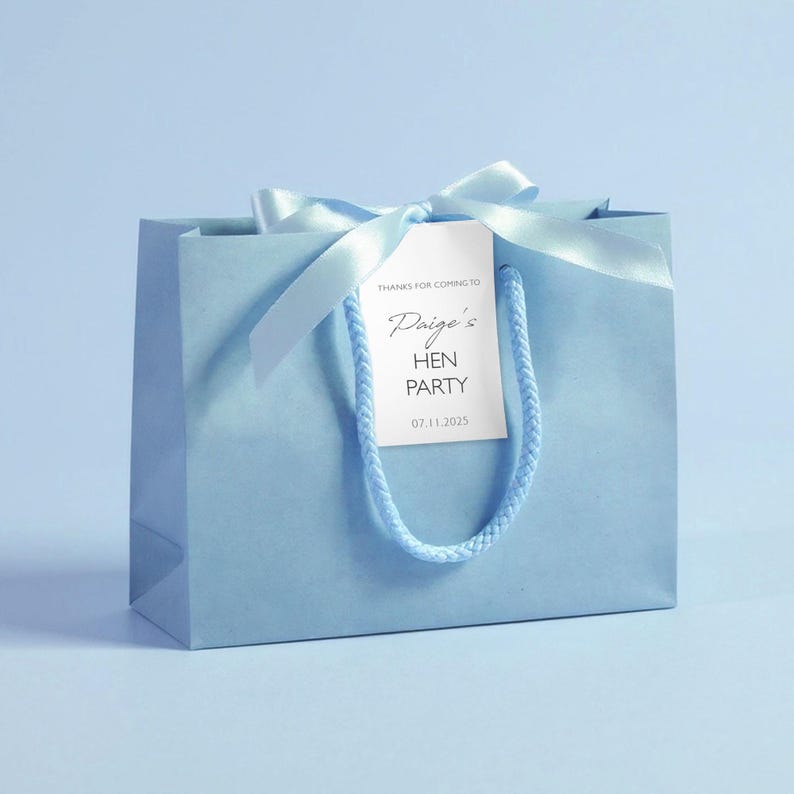 May include: A light blue gift bag with a matching ribbon and tag. The tag reads "Paige's HEN PARTY 07.11.2025" in elegant script. The bag has a twisted cord handle, perfect for party favors.