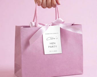 May include: A pink gift bag with matching handles and a white tag tied with a satin ribbon. The tag reads "Thanks for coming to Chloe's Hen Party 07.11.2025". The bag is held by a hand.