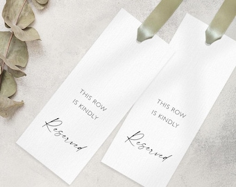 May include: Two white rectangular tags with the words "THIS ROW IS KINDLY Reserved" printed in black. Each tag has a light green ribbon attached at the top. The tags are on a light grey surface.