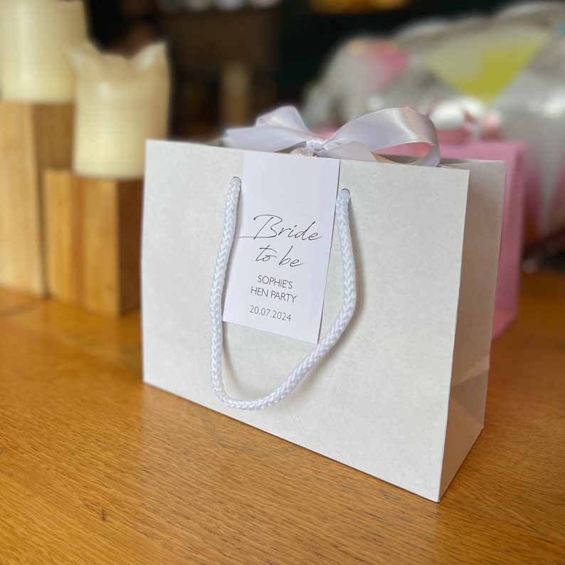 Personalised hen party gift bags with custom tags and ribbons, perfect for adding a special touch to hen do favours. Made from 100% recycled paper with reinforced bases and soft rope handles, these elegant bags can be customised with names, dates, or messages. Ideal for presenting gifts or party favours in style.