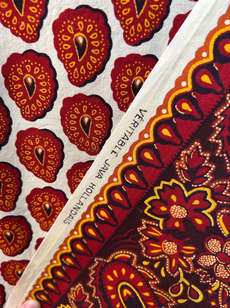 May include: Close-up of two fabric swatches. One features a repeating pattern of red, yellow, and black teardrop shapes on a cream background. The other displays a floral design with the text "VERITABLE JAVA HOLLANDAIS" along the edge.