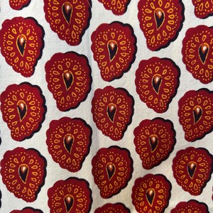 May include: Close-up of a fabric with a repeating pattern of stylized red fruit shapes. Each shape has a dark outline, a yellow dotted border, and a central teardrop design. The background is a light cream color.