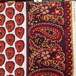 May include: A fabric with two distinct patterns. One side features a repeating pattern of red strawberry-like shapes on a white background. The other side showcases a paisley design in red, yellow, and brown. The text "GUARANTEED DUTCH" is visible.